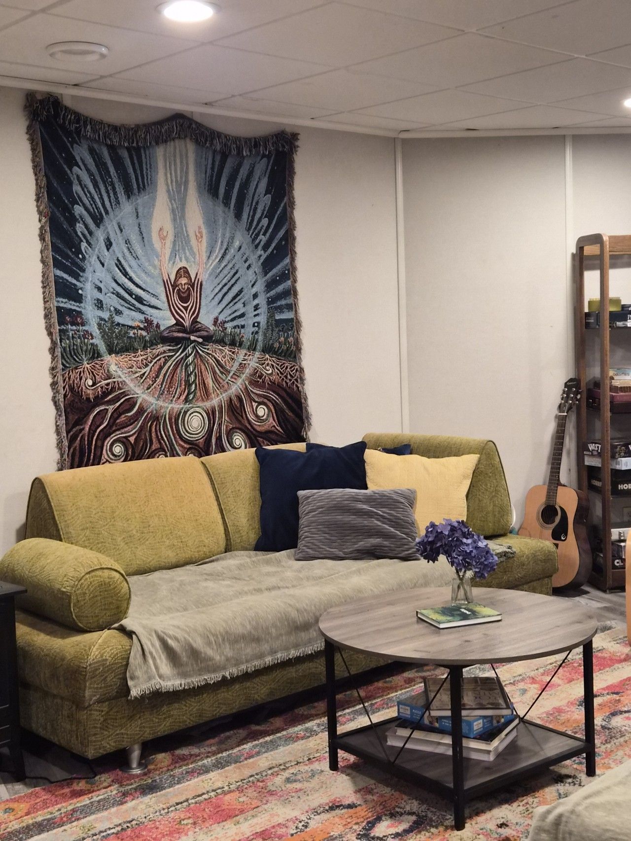 Un salon avec un canapé, une table basse ronde, une tapisserie et une guitare.