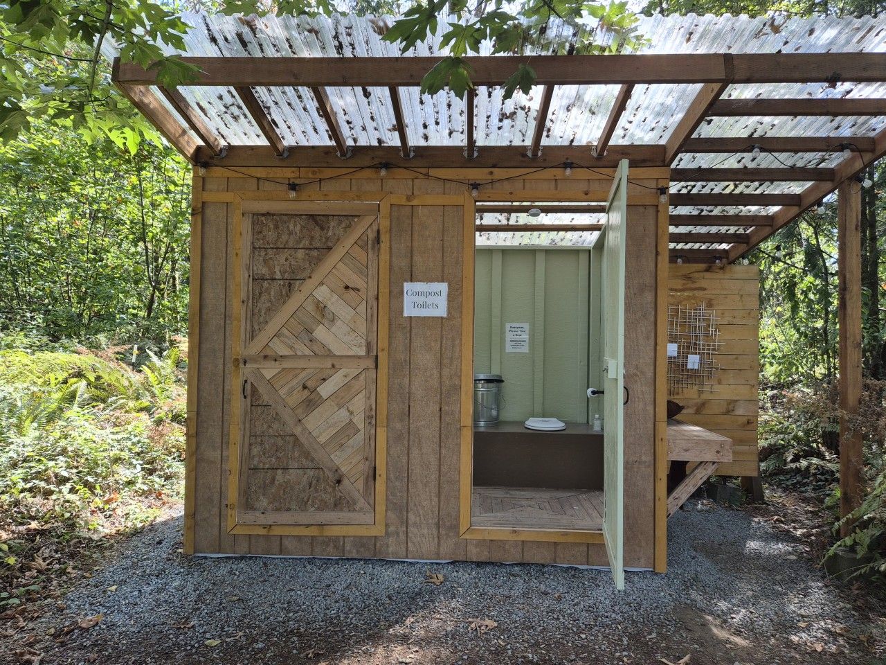 Una construcció de fusta amb una porta, un rètol que indica compost i lavabos, i una petita cadira.