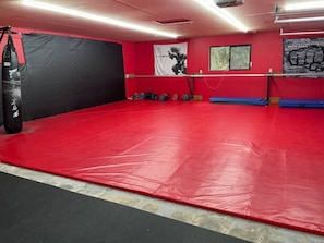 A gym with red flooring, a punching bag, and exercise mats.