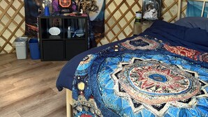 Una habitación acogedora con una cama, un tapiz en la pared, una mesita con objetos y suelo de madera.