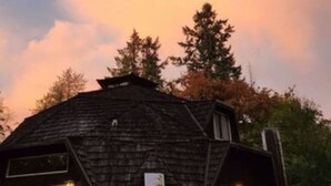 Un edificio de dos plantas con techo oscuro y una chimenea visible.