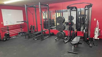 A gym with weightlifting equipment, benches, and a whiteboard on the wall.