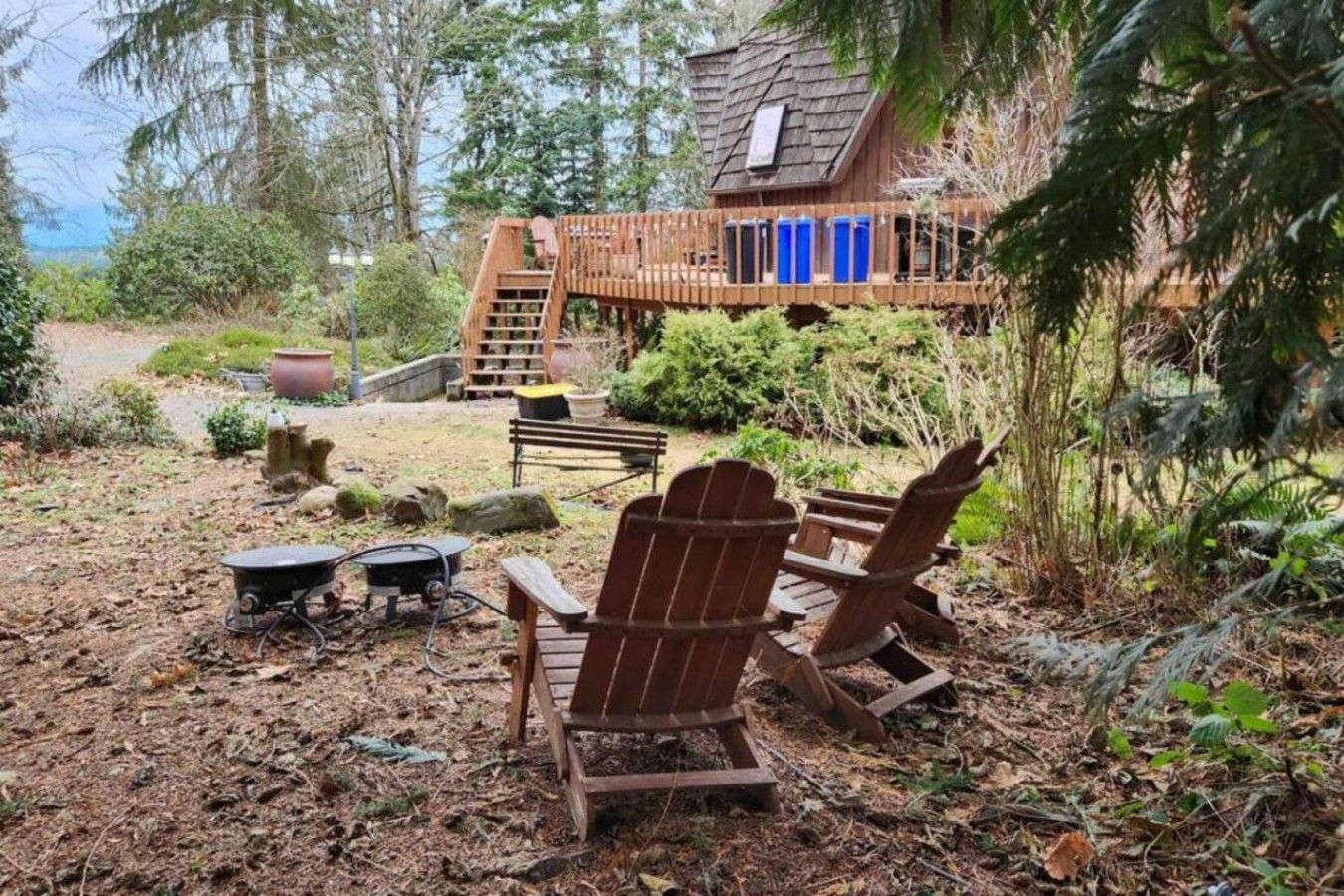 A wooden deck with Adirondack chairs, a fire pit, and a wooden structure with blue doors.