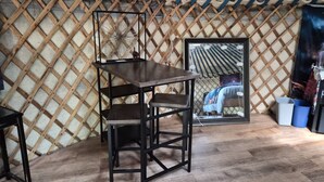 Una habitación con un muro de celosía de madera, una mesa de madera oscura con una silla, un espejo enmarcado y un cubo azul.