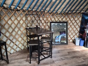 Una habitación con un muro de celosía de madera, una mesa de madera oscura con una silla, un espejo enmarcado y un cubo azul.