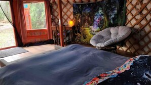 Una habitación acogedora con una cama, un sillón y un tapiz que representa un paisaje boscoso.