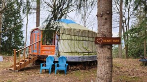 Una estructura cubierta con una escalera que conduce a una puerta naranja, dos sillas azules y un letrero que dice "Heart Yurt".