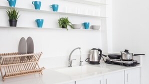 A modern kitchen with white cabinets, a stainless steel sink, a kettle, a frying pan, and a rack holding plates and bowls. - Port 2 Bedroom with 2 showers apartment (Tel Aviv)
