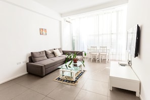 A modern living room with a sofa, a glass coffee table, a white desk, and a potted plant.