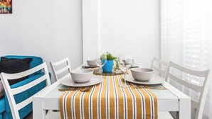 A dining area with a white table set for two, a blue vase with greenery, and a striped tablecloth. - Port 2 Bedroom with 2 showers apartment (Tel Aviv)