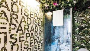 A bathroom with a shower, a towel hanging on the wall, and a wall with a repeating pattern of the word "PARADISE". - Port 2 Bedroom with 2 showers apartment (Tel Aviv)