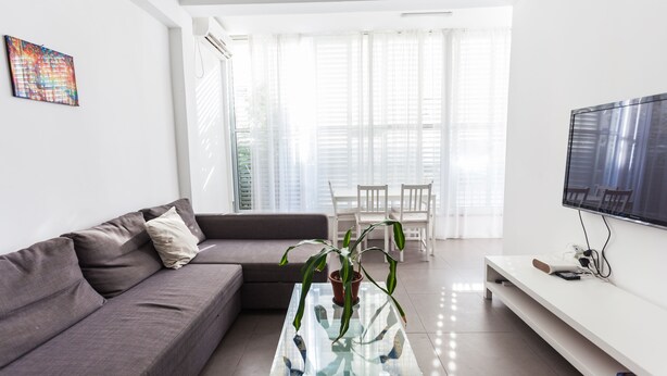 A modern living room with a glass coffee table, grey sofa, and a flat-screen TV. - Port 2 Bedroom with 2 showers apartment (Tel Aviv)