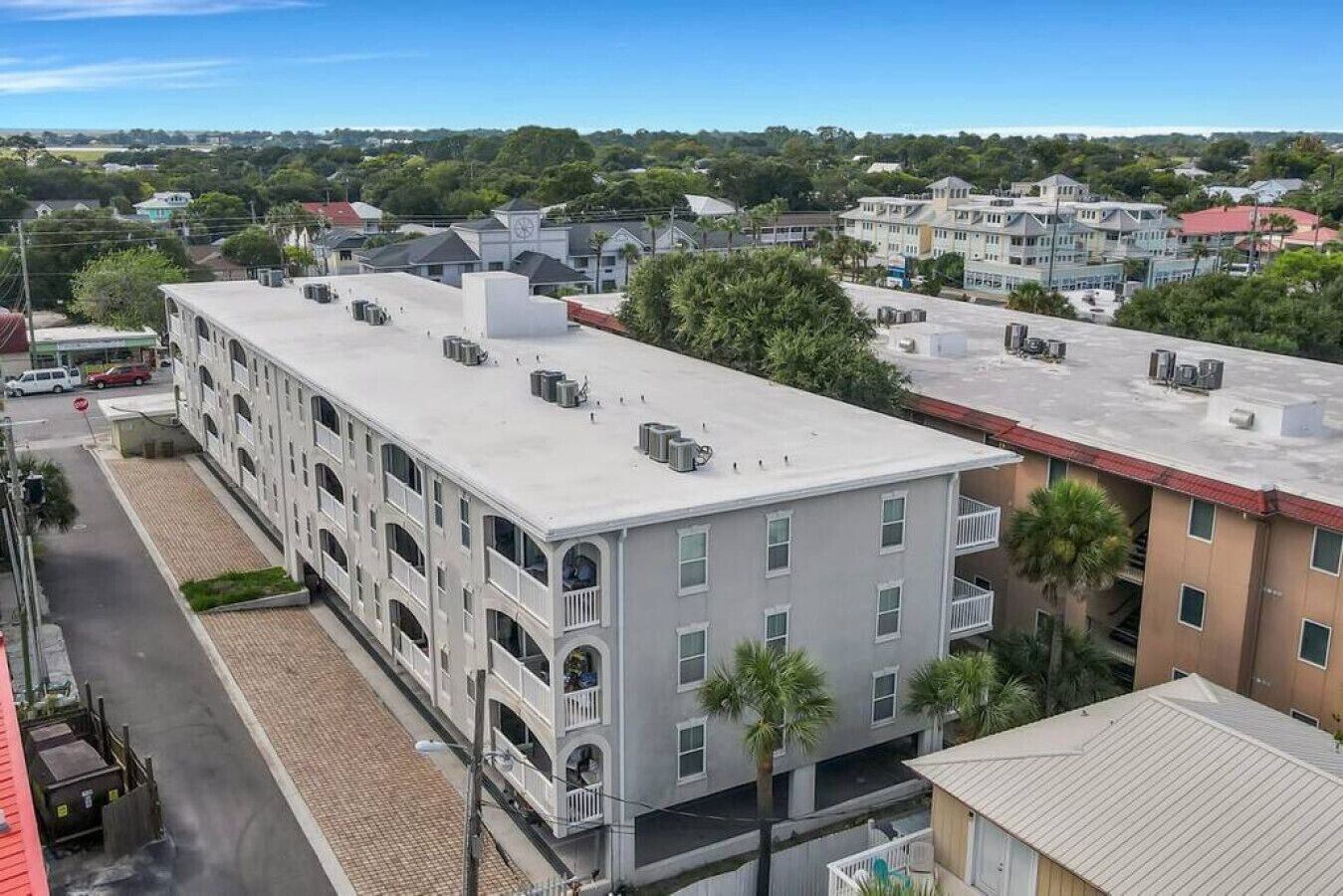 A multi-story building with a flat roof, air conditioning units, and a brick-paved ground floor.