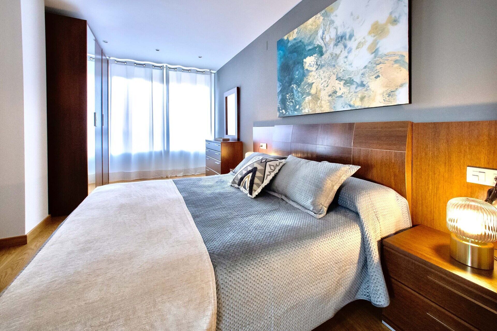Un dormitorio moderno con una cama grande, una mesita de noche, una lámpara de pared y un cuadro abstracto de grandes dimensiones.