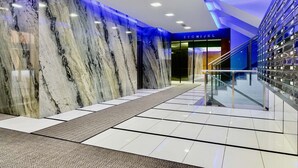 Un hall d’entrée moderne avec des murs en marbre, une moquette à motifs et une rambarde en verre.