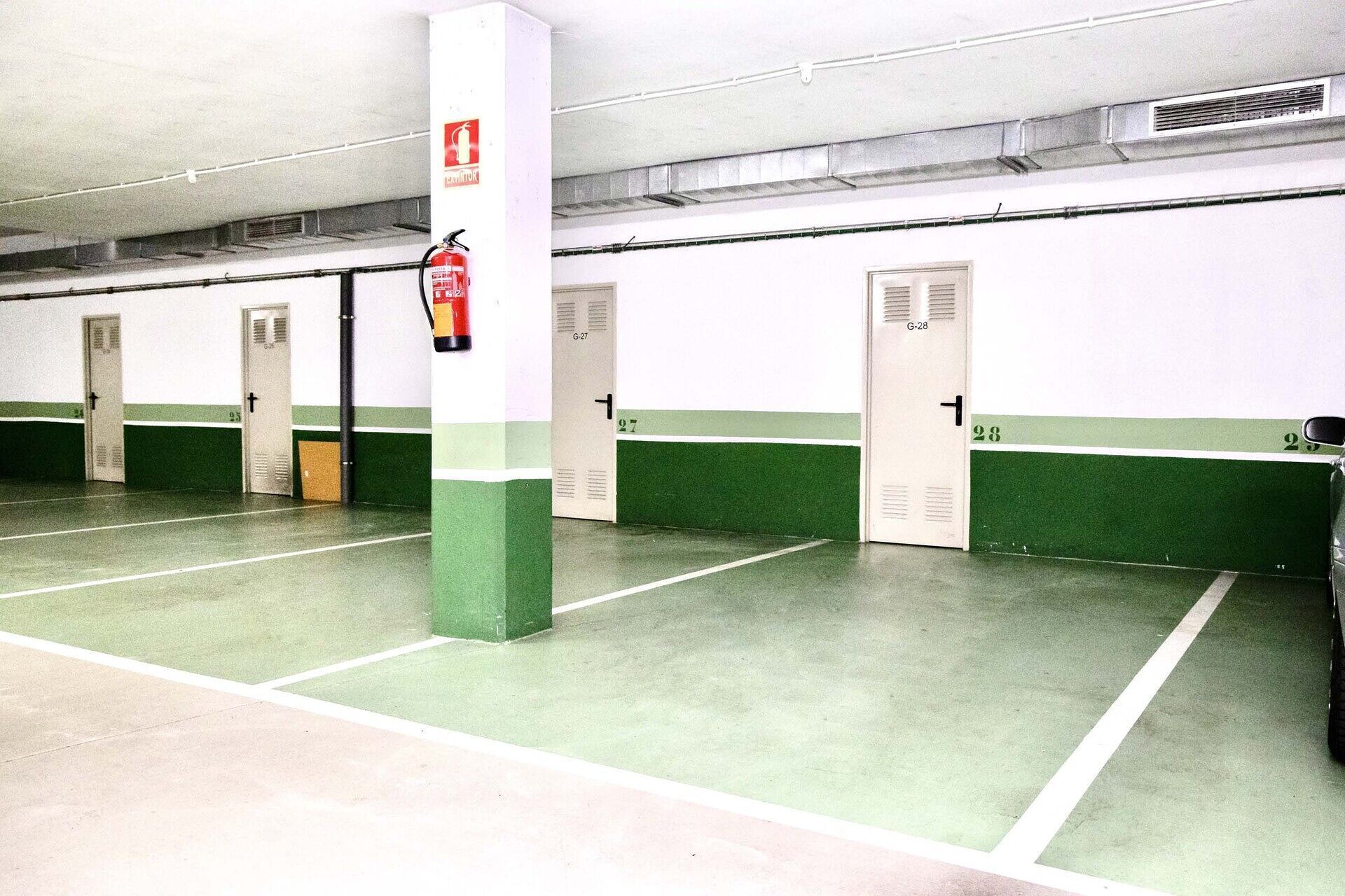 A parking garage with multiple parking spaces, fire extinguishers, and doors labeled with numbers.