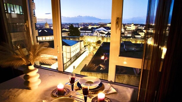 Une table dressée pour deux personnes, avec des bougies et une vue sur le paysage urbain par la fenêtre.