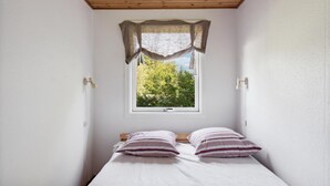 Une petite chambre avec un lit simple, une fenêtre donnant sur des arbres et un plafond en bois.