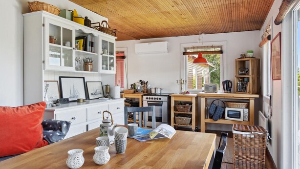 Une cuisine chaleureuse avec des poutres en bois, un meuble blanc aux portes vitrées, une cuisinière et une fenêtre donnant sur un paysage verdoyant.