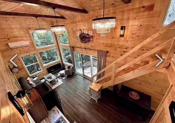 A wooden cabin interior with a dining area, kitchen, and a staircase leading to a loft.