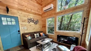 A cozy cabin interior with a blue door, wooden walls, a sofa with cushions, a coffee table, and a fireplace. - Boxcar Cabin - Hot Tub, Fire Pit, Train-Theme Stay (Stanton)
