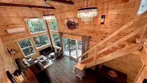 A wooden cabin with a kitchen, dining area, and a staircase leading to an upper level. - Boxcar Cabin - Hot Tub, Fire Pit, Train-Theme Stay (Stanton)