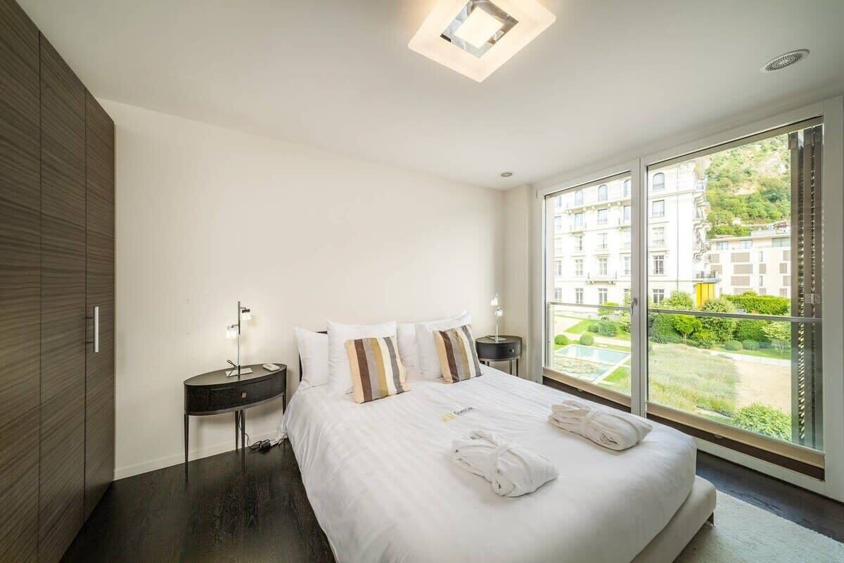 Une chambre d’hôtel moderne dotée d’un grand lit, d’une table de chevet, d’une commode et offrant une vue sur la ville grâce à de grandes fenêtres.