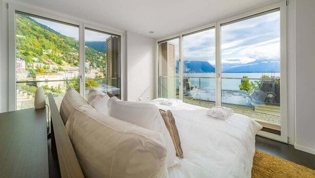 A bedroom with a large window offering a view of a mountainous landscape and a body of water. - Luxury Apartment Lake view in Montreux by GuestLee (Montreux)