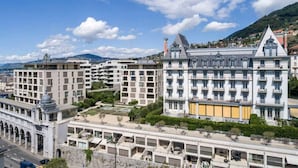 A modern hotel with multiple floors, a central courtyard, and a mountain backdrop. - Luxury Apartment Lake view in Montreux by GuestLee (Montreux)