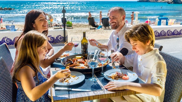 Un grupo de personas cenando en una mesa al aire libre con vista a la playa y al océano.