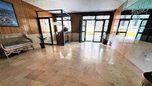 Un hall espacioso con piso de mármol pulido, un sofá de mimbre y un separador de vidrio.