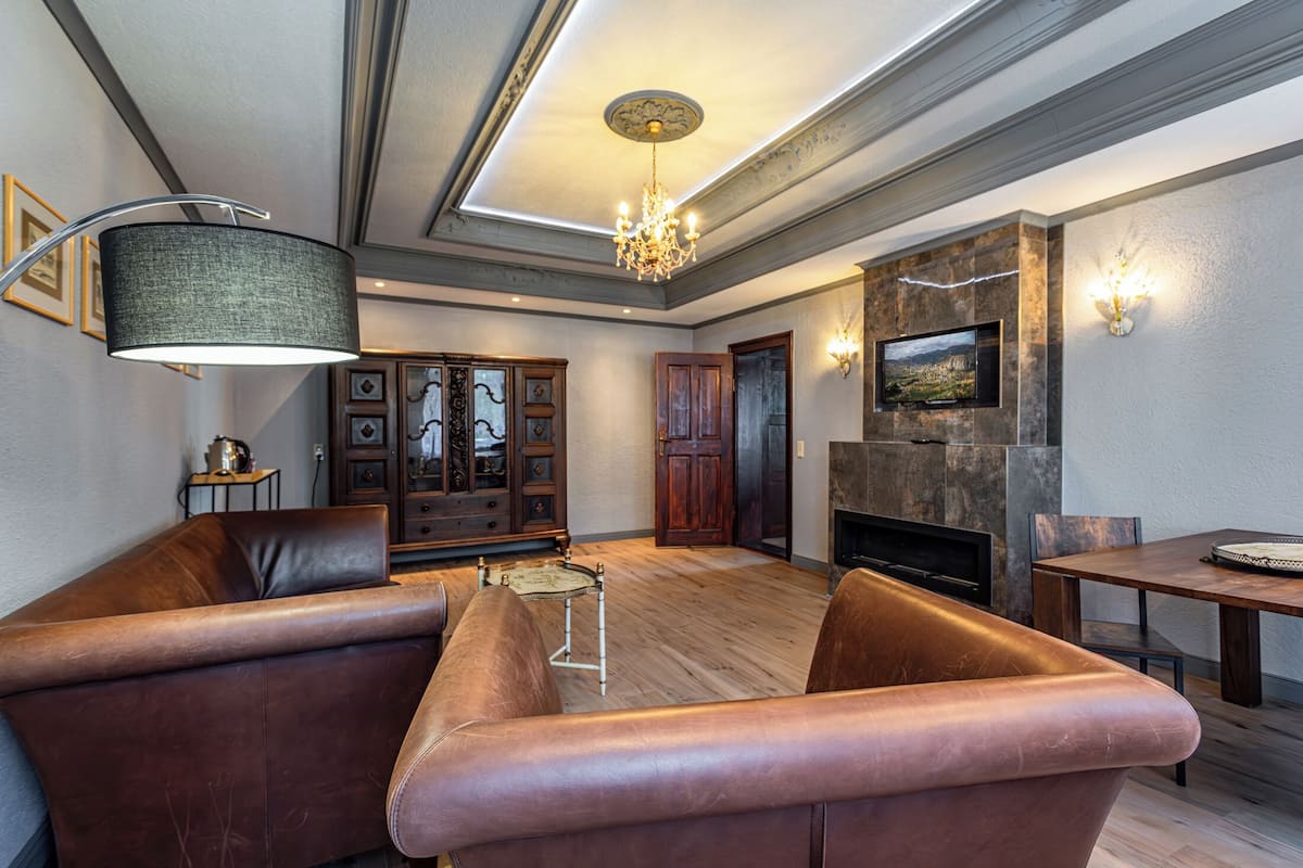 A spacious living room with leather sofas, a chandelier, a fireplace, and a television mounted on the wall.