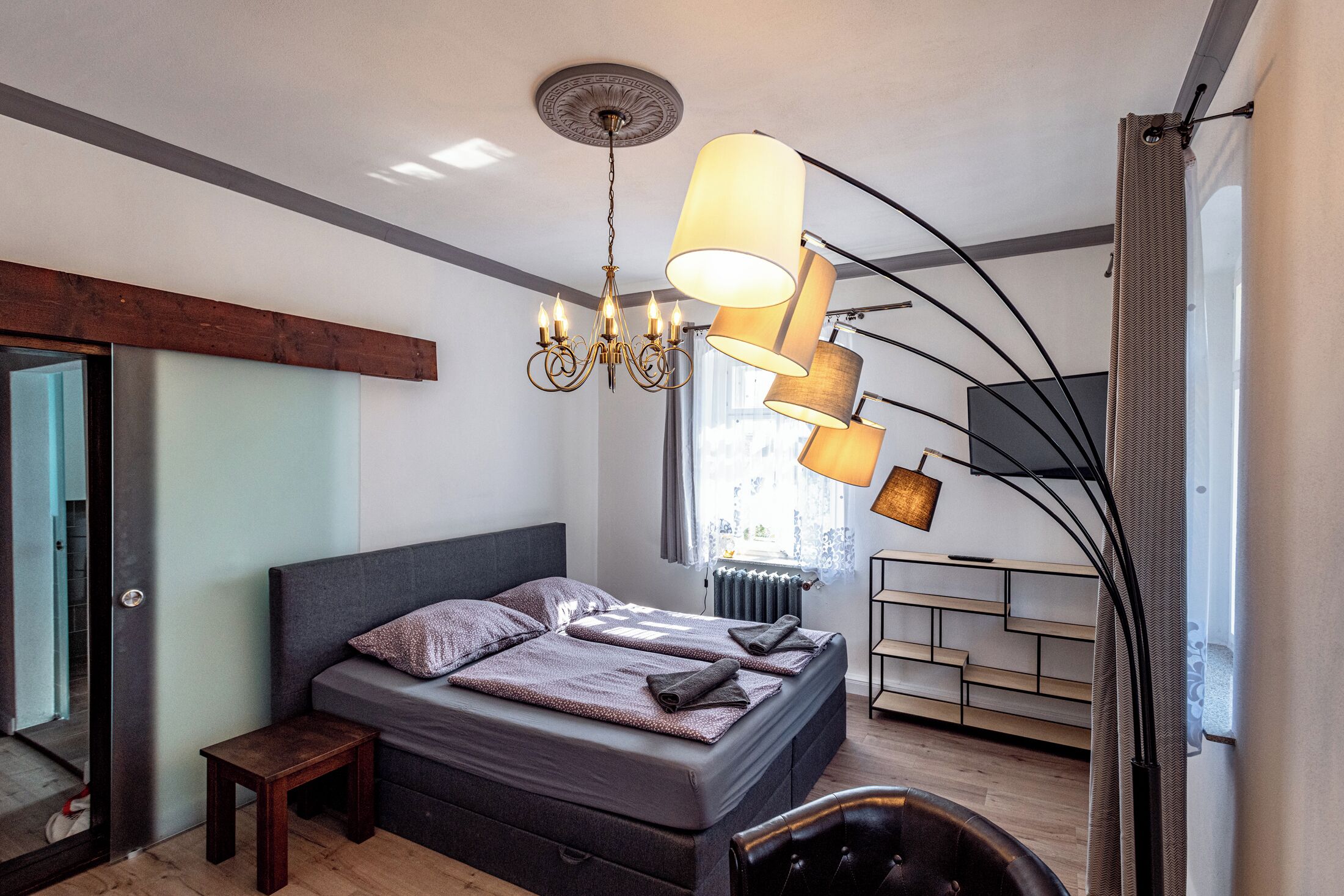 Ein modernes Schlafzimmer mit einem großen Bett, einer Chandelüster und einer Stehlampe.