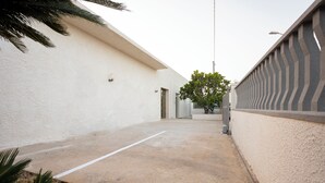 A narrow concrete pathway flanked by white walls, leading to a door. - SALUTAMU (Misiliscemi)