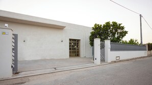 A building with a gated entrance, a small window, and a tree in front. - SALUTAMU (Misiliscemi)