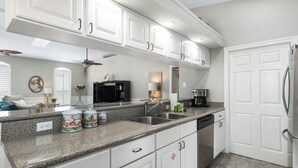 A modern kitchen with white cabinets, granite countertops, a dishwasher, and a refrigerator. - Remodeled home minutes to the beach! (Miramar Beach)