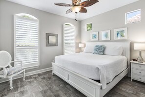 Une chambre à coucher comprenant un lit, une chaise, une table de chevet, une lampe et un ventilateur de plafond.