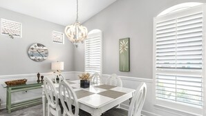 A dining area with a white table and chairs, a chandelier, a clock, and artwork on the walls. - Remodeled home minutes to the beach! (Miramar Beach)
