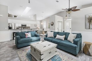 Un salon moderne avec deux canapés de couleur turquoise, une table basse blanche et un ventilateur de plafond.