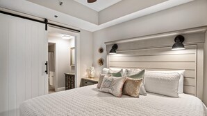 Un dormitorio con una cama grande, una mesita de noche, un aparador y una puerta corredera que da a otra habitación.