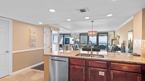 A modern kitchen with granite countertops, stainless steel appliances, and a view to the living area. - Updated beach condo with stunning views! (Miramar Beach)