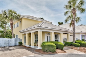 A yellow building with a tiled roof, columns, and a white fence.