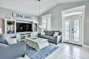 A living room with a TV, grey sofa, white entertainment unit, and a sign reading "THE CRAB SHACK".