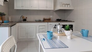 Eine moderne Küche mit weißen Schränken, einer Arbeitsplatte mit Kaffeemaschine, einer Pflanze und zwei blauen Tassen.