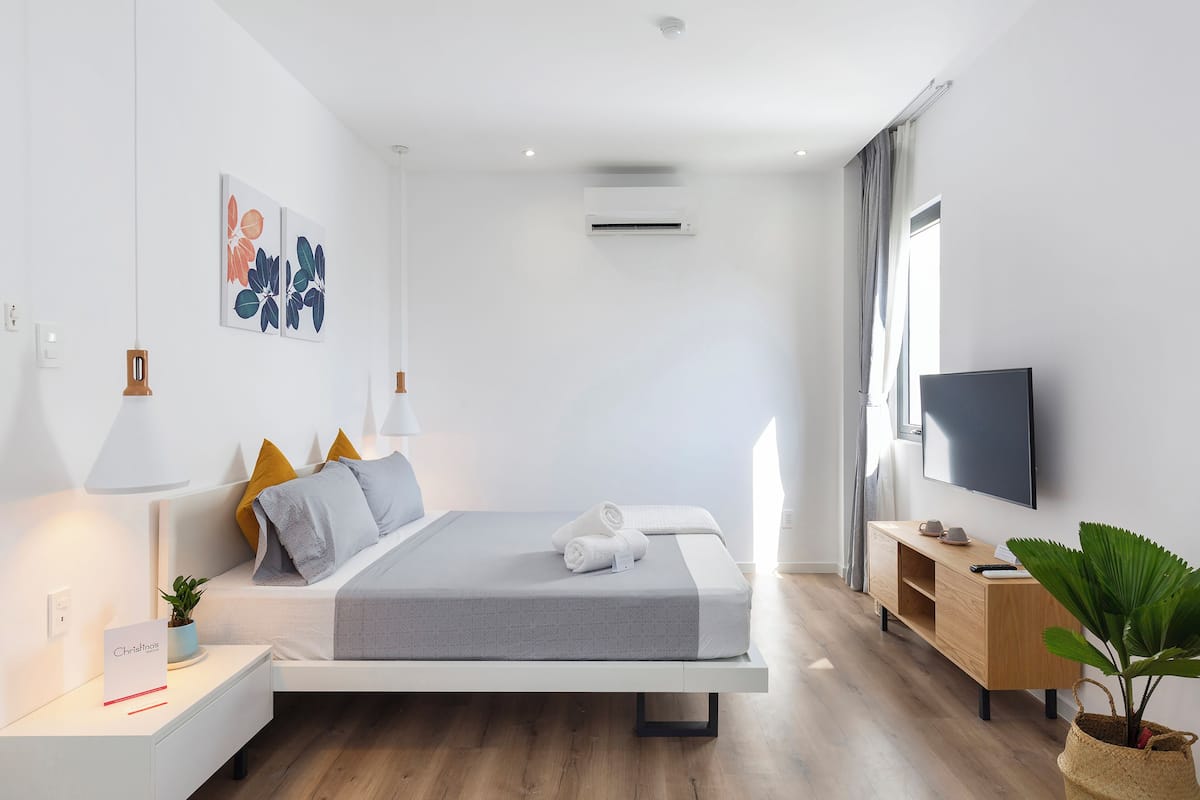 A modern bedroom with a bed, bedside tables, a TV, and a potted plant.