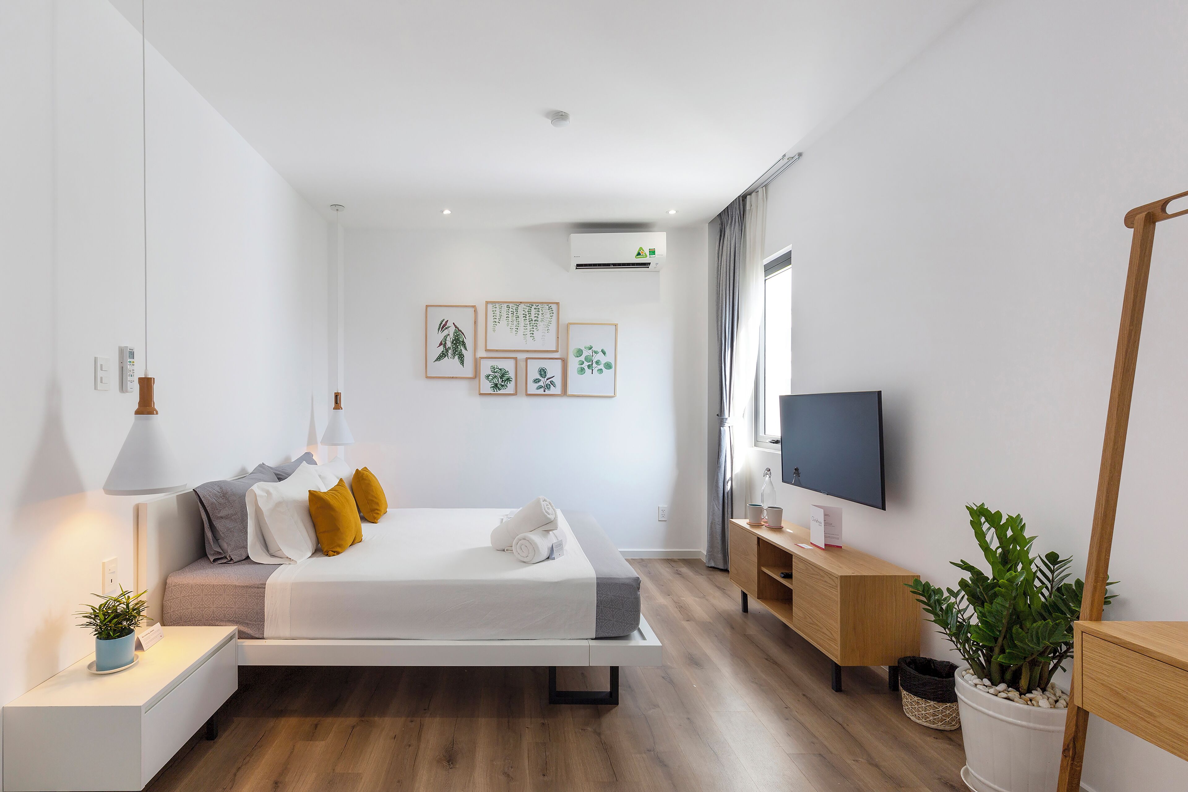 Ein modernes Schlafzimmer mit Bett, Nachttischen, einem Fernseher und einer Topfpflanze.