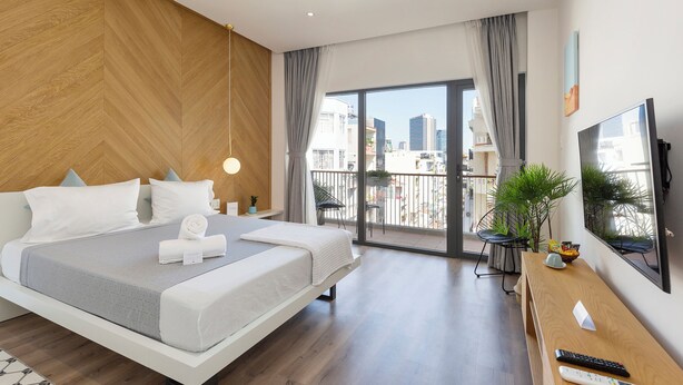 Quarto de hotel moderno com uma cama grande, televisão, varanda com vista para a cidade e piso de madeira.