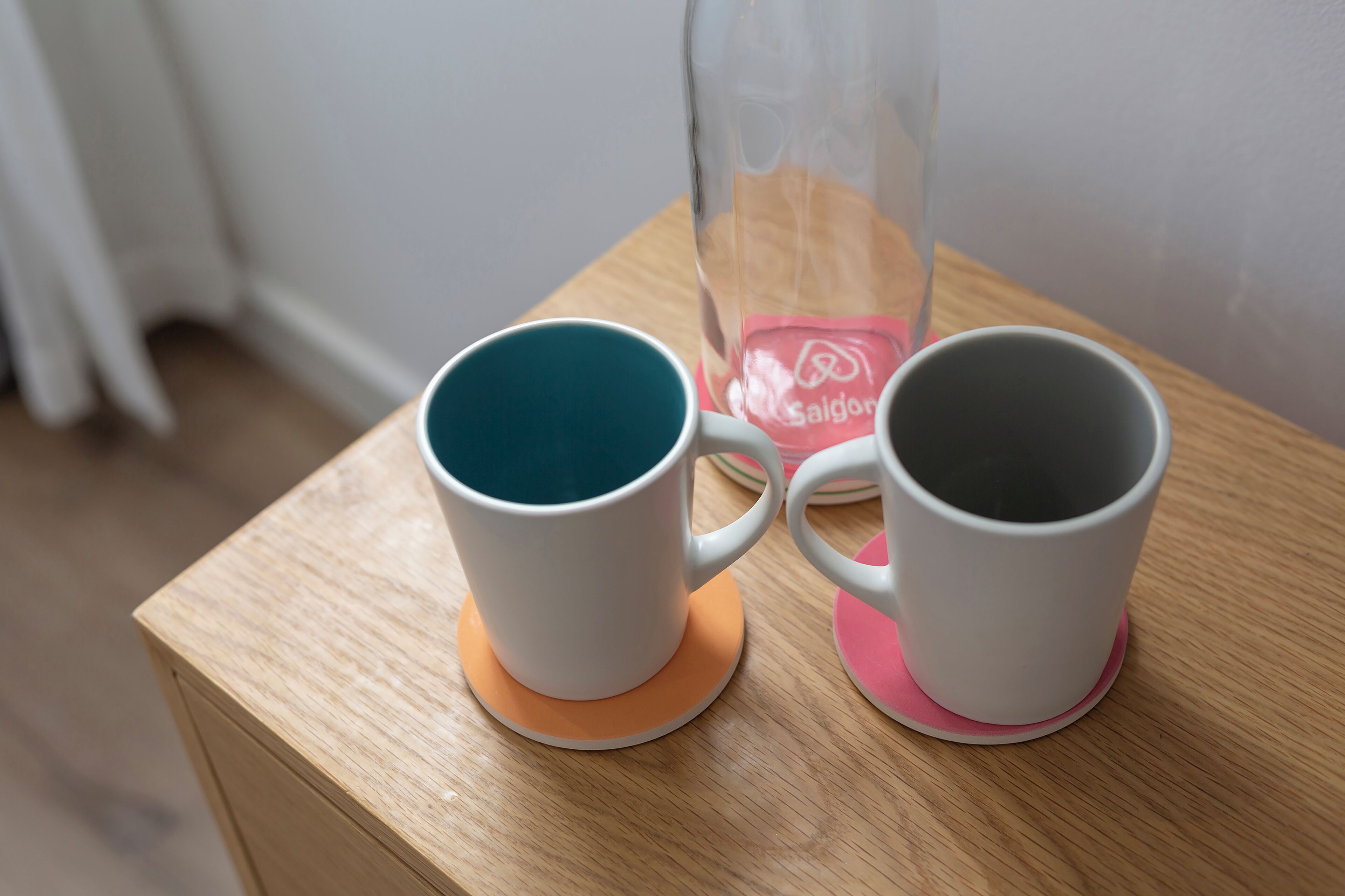 Deux tasses en céramique blanche sont posées sur une table en bois, et une bouteille en verre se trouve à l’arrière-plan.