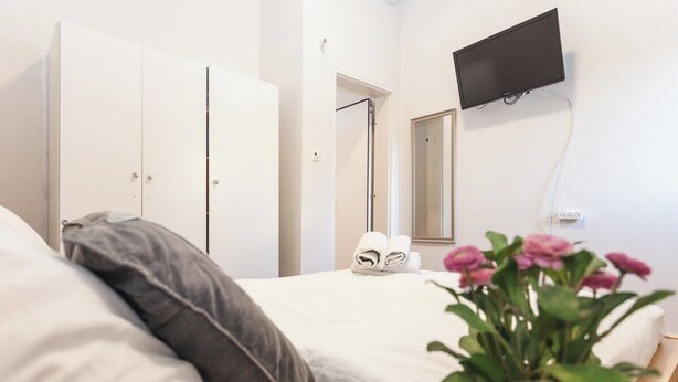 A hotel room with a bed, a TV mounted on the wall, a wardrobe, and a mirror. - Ben Yehuda By theLight apartment (Tel Aviv)