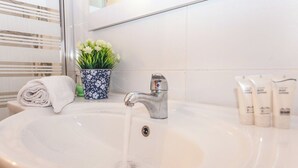 A bathroom sink with running water, a potted plant, a towel, and toiletries. - Ben Yehuda By theLight apartment (Tel Aviv)